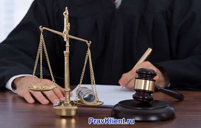 Судья пишет на листке бумаги, рядом стоят весы Фемиды, деревянный молоточек